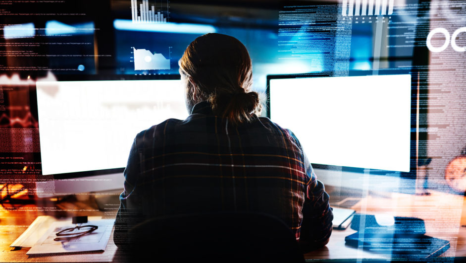 Working hard at it Rearview shot of an unrecognizable male programmer working late at night in the office