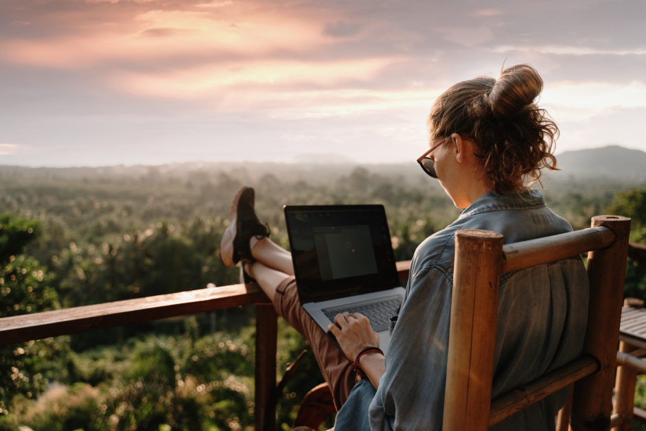 Young business woman working at the computer in cafe on the rock. Young girl downshifter working at a laptop at sunset or sunrise on the top of the mountain to the sea, working day. work from anywhere