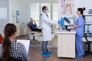 professional-doctor-asking-dental-xray-before-examining-patient-while-people-waiting-receptio